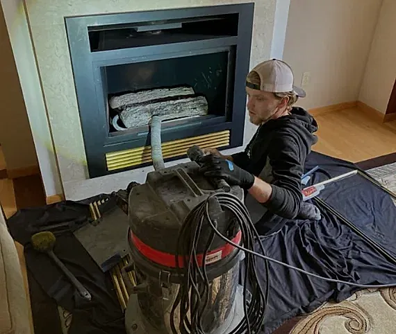 ABD technician vacuuming dust and debris from a gas fireplace insert in a customer's home