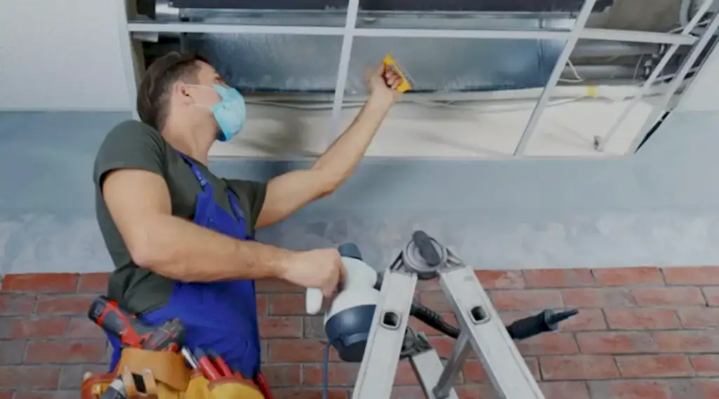 Technician on a ladder sanitizing ceiling air ducts in Ashburn, VA