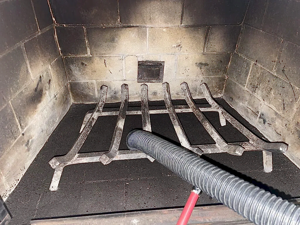Vacuum hose clearing soot from a fireplace firebox and grate during an ABD chimney cleaning