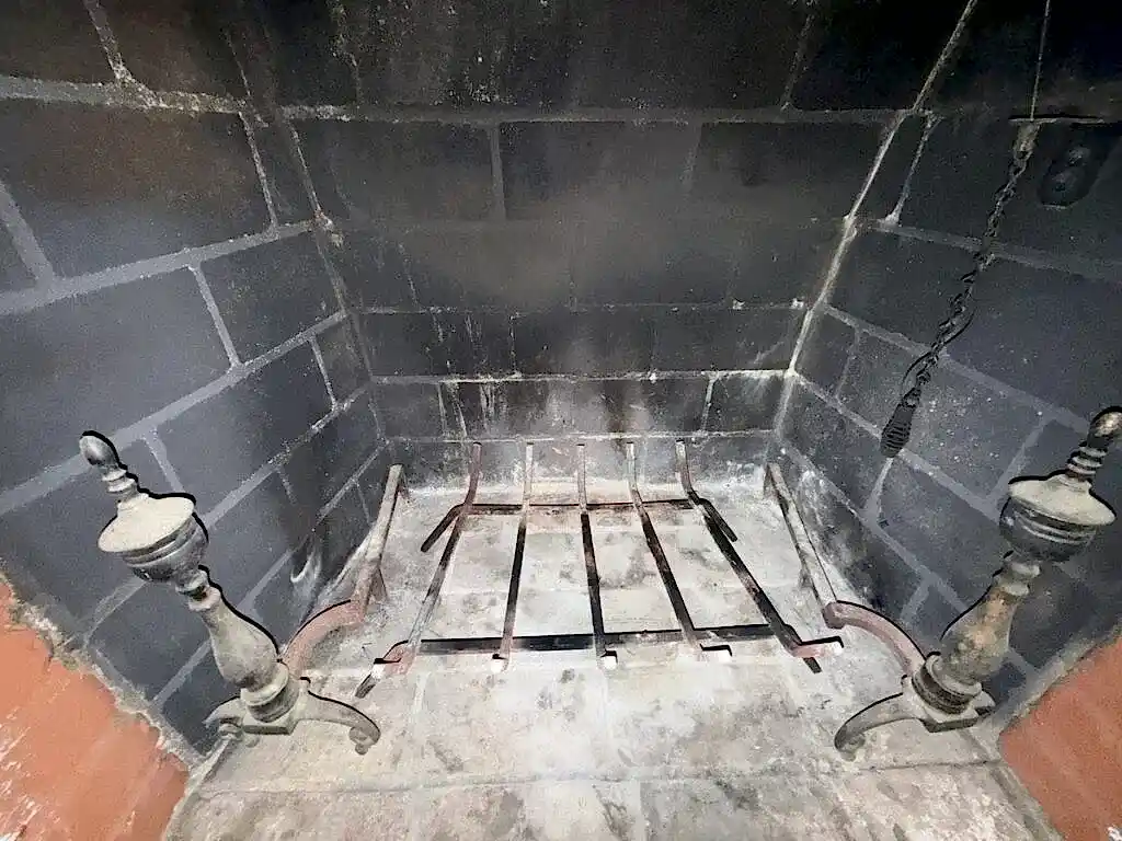Clean firebox of a wood-burning fireplace with a grate and brass andirons on an ABD chimney cleaning job