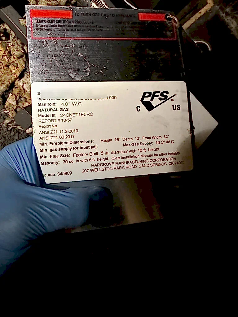 Technician in a blue glove holding a gas log set rating plate during an ABD gas fireplace inspection
